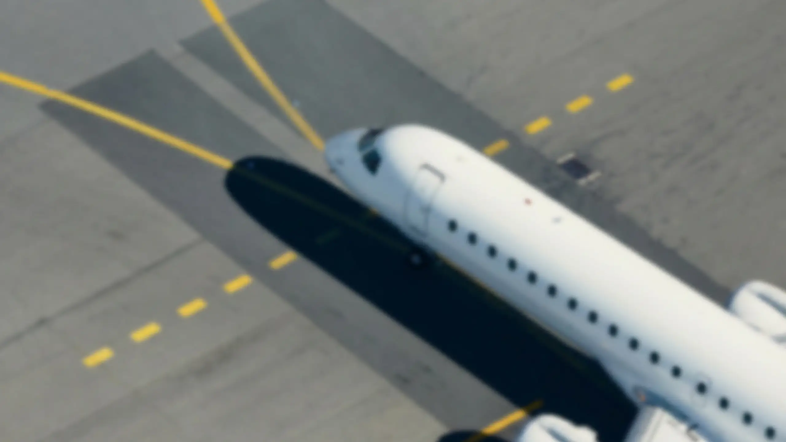 Blurred aerial view of passenger plane on airport apron with yellow markings and clear shadow