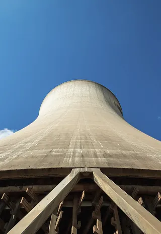 An interior view of a power plant cooling tower, taken from below, showing the curved concrete wall and internal structure of supporting scaffolding.