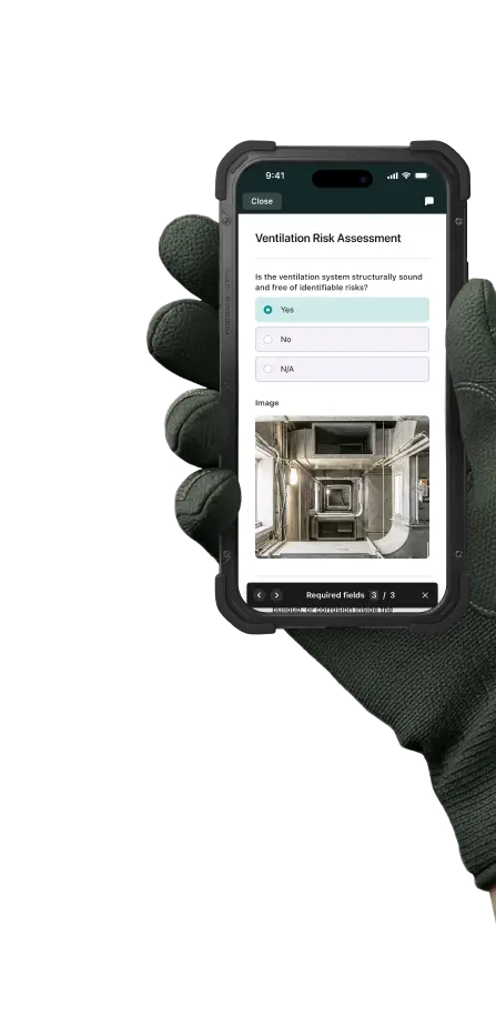 A hand in a work glove holds a mobile phone with the Ventilation Risk Assessment checklist open in the Fluix app.