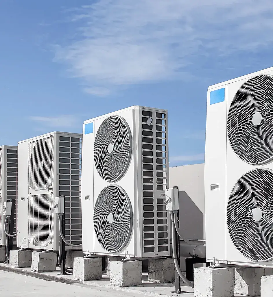 A row of large commercial HVAC units with two round fans each, mounted on concrete pillars under a bright blue sky