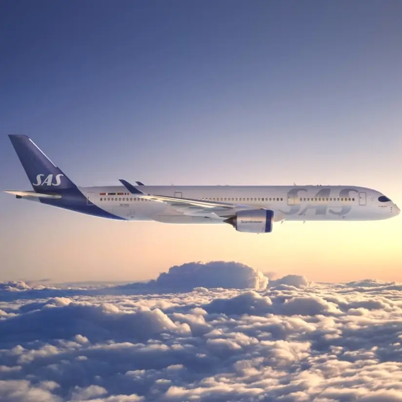 A plane with the SAS logo in the sky at sunset.