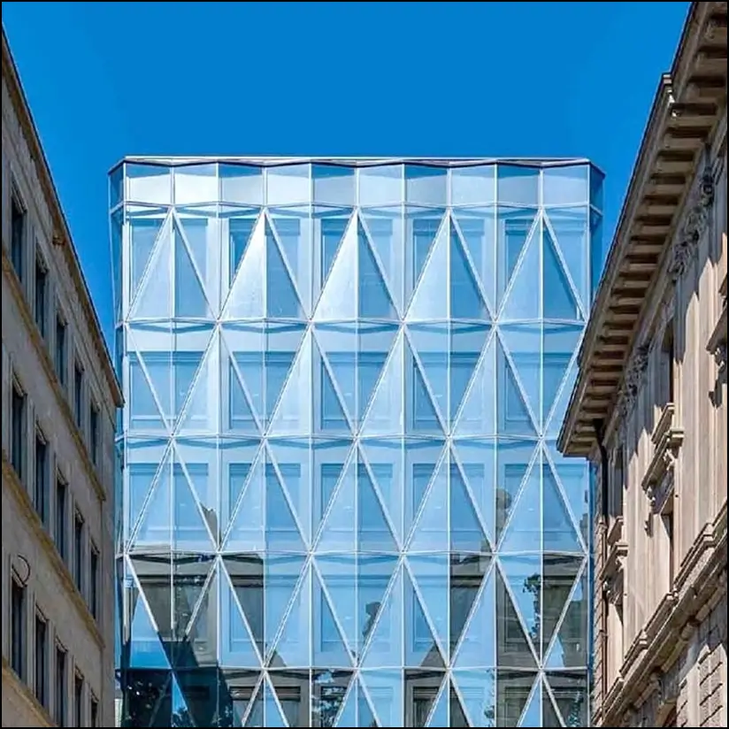 A high-rise building with a glass facade set against a backdrop of older residential buildings.