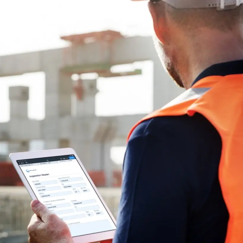 A technician at a construction site is holding a tablet with the Fluix app.