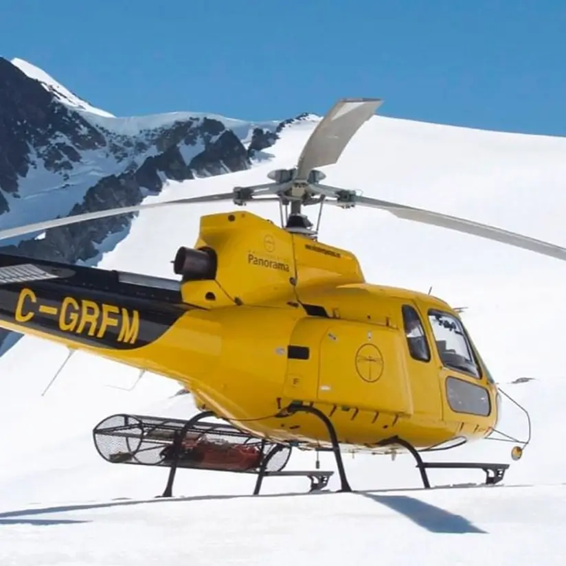 A yellow helicopter with the Panorama Helicopters logo in the snowy mountains.