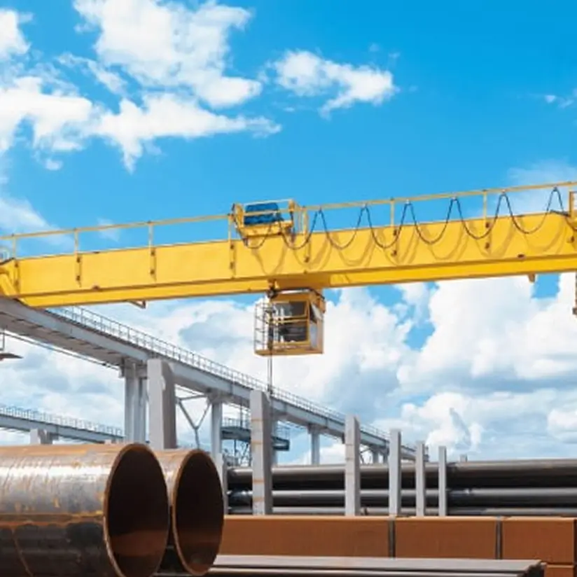 A yellow industrial crane loads large-diameter pipes against a blue sky.